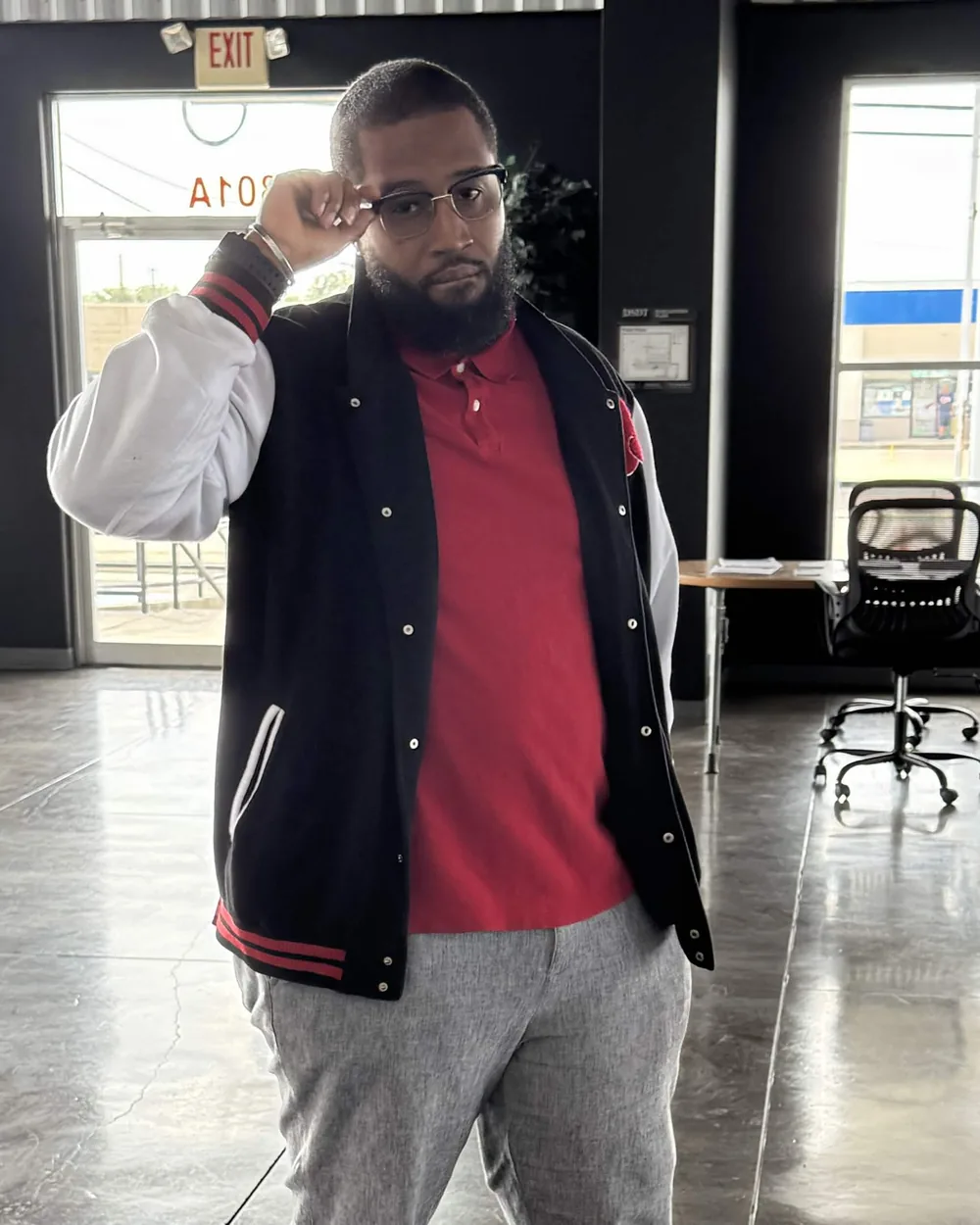 Mavinga Warner in a black and white varsity jacket, adjusting his glasses.